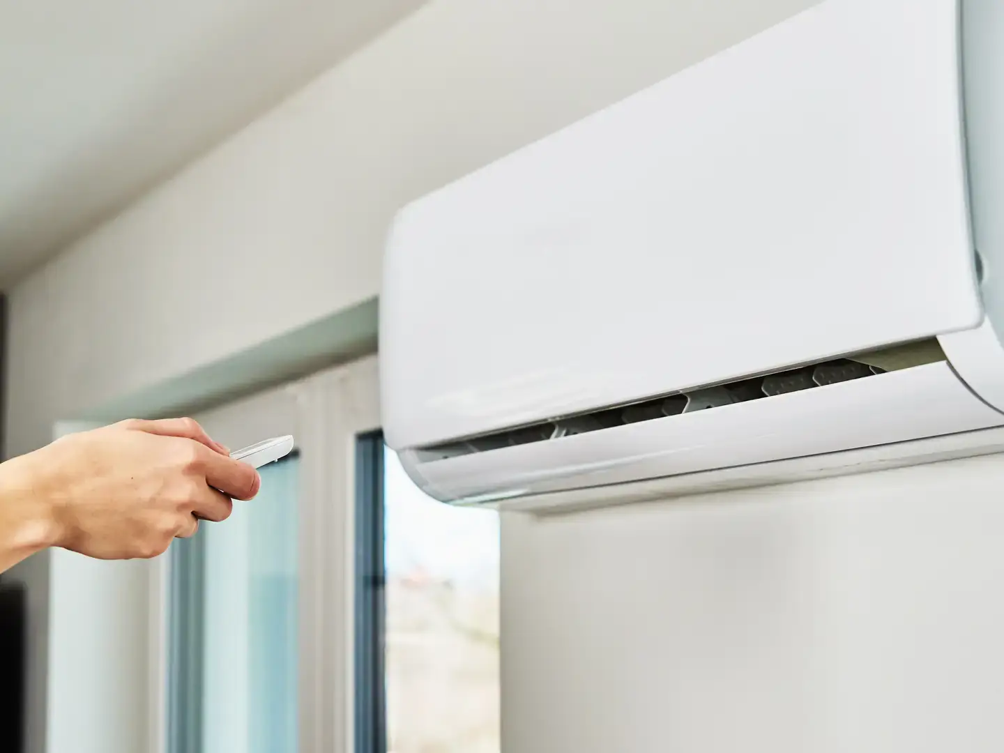 Main réglant une climatisation murale avec sa télécommande dans un logement